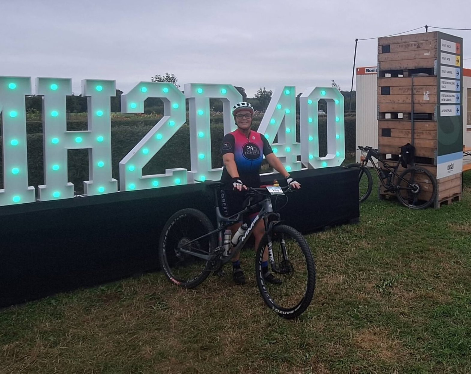 Alice poseert met haar mountainbike voor de grote verlichte MH2D-letters op het evenemententerrein