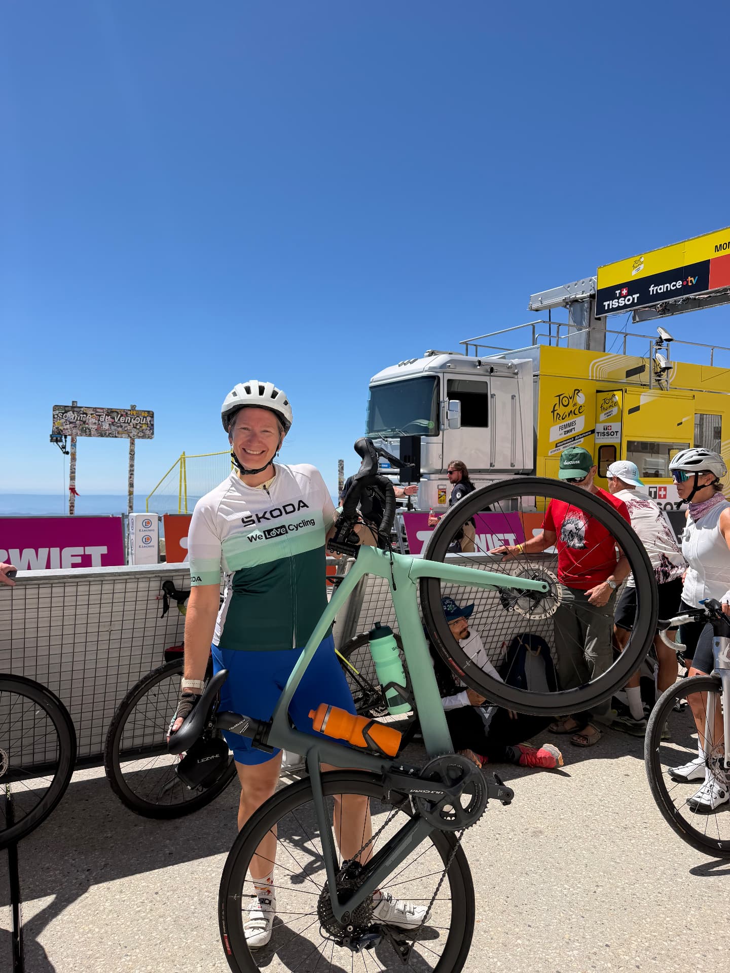 Claire lacht in de camera terwijl ze haar racefiets omhoog houdt op de top van de Mont Ventoux