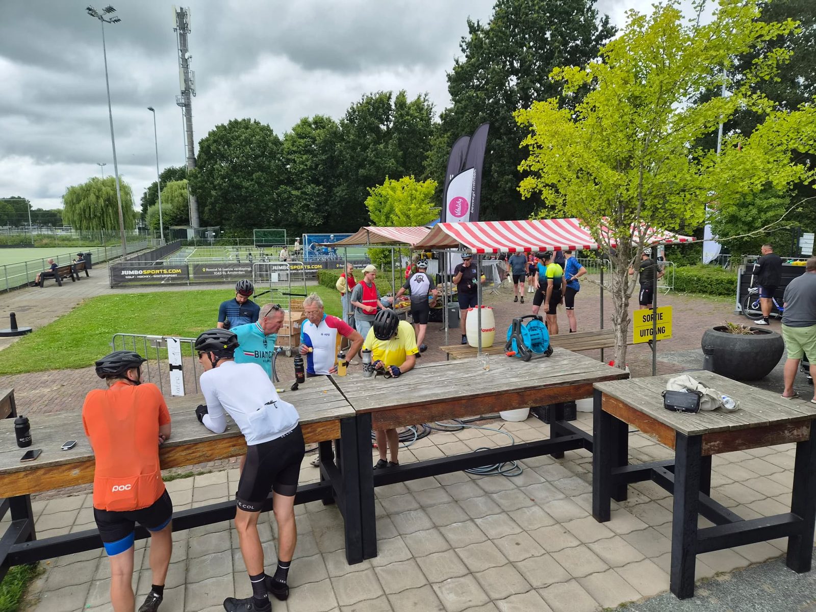 Deelnemers van de Tour d’Utrecht pauzeren bij een rustpost met picknicktafels