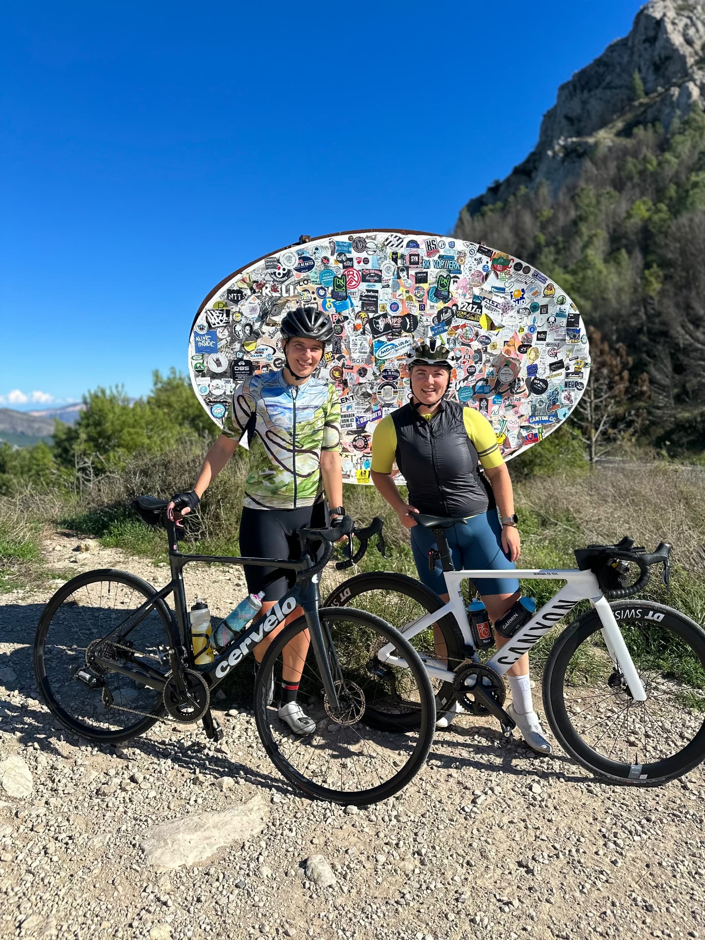 Two Cyclingwomen with road bikes at the famous sticker board on the Coll de Rates in Spain