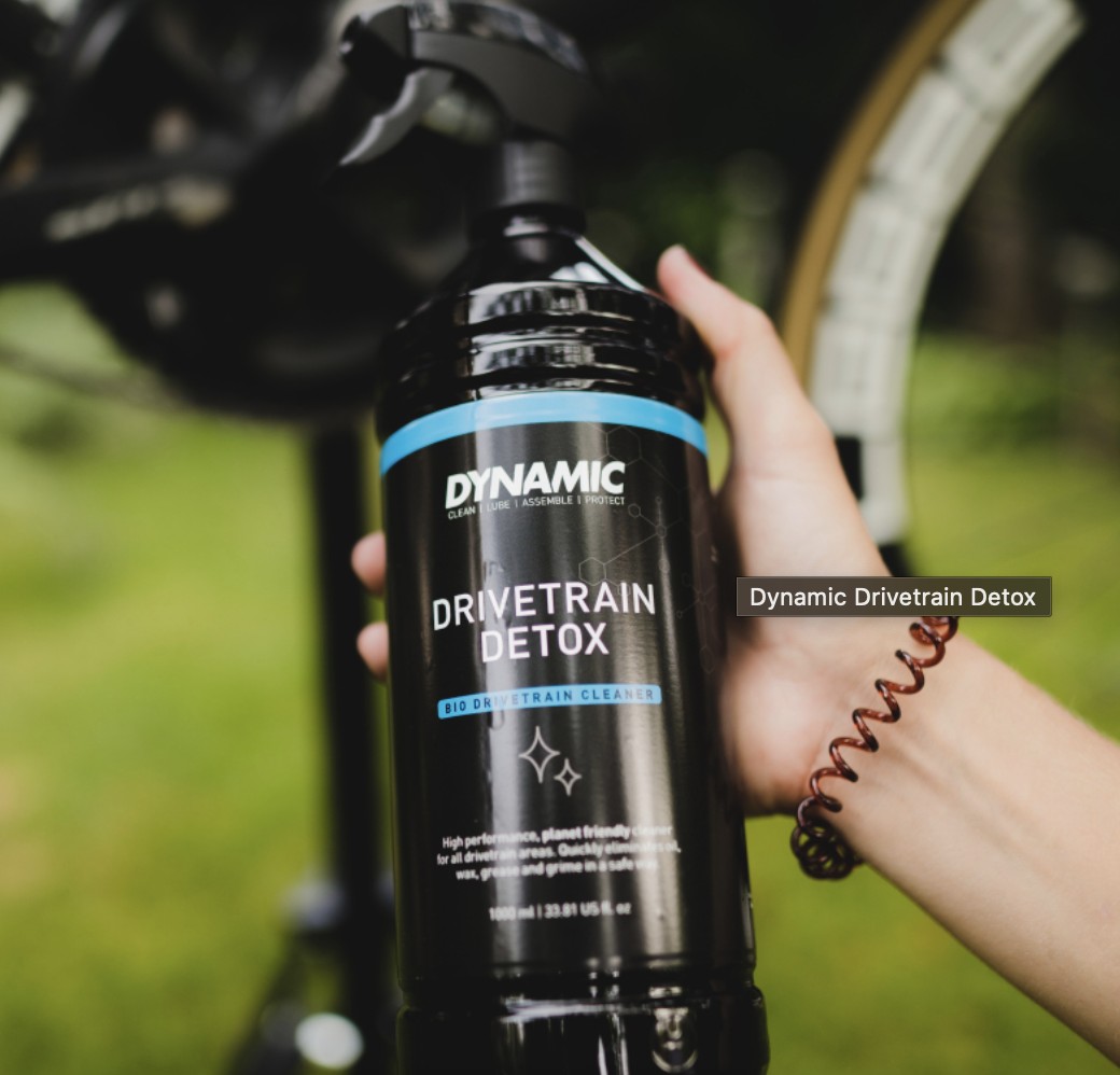 Hand houdt een fles Dynamic Drivetrain Detox omhoog: een biologische reiniger voor ketting, voorbladen en cassette