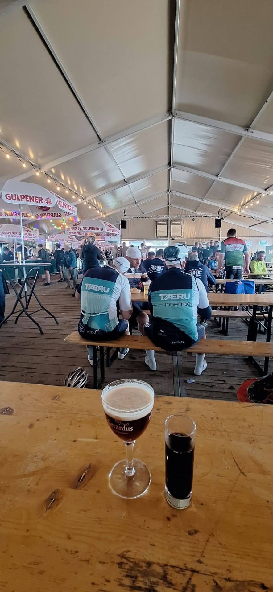 Gezellige festivaltent met fietsers en een glas Bernardus op tafel na de finish van de MH2D