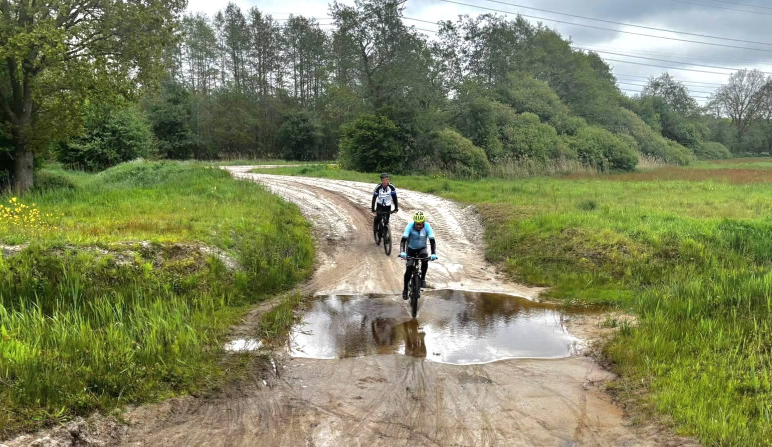 Mountainbikers fietsen door een grote plas water op het militair oefenterrein bij Assen