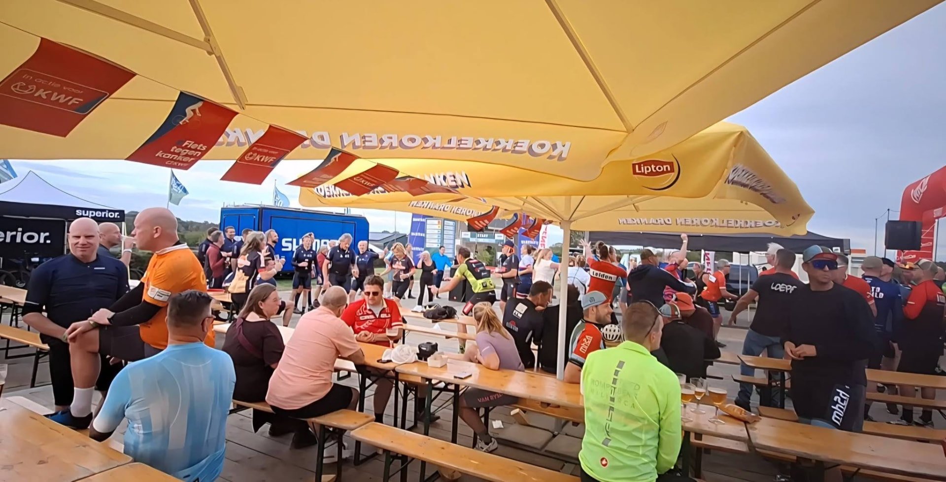 Druk bezocht terras met deelnemers onder parasols op het evenemententerrein van de Mergel Heuvelland 2 Daagse