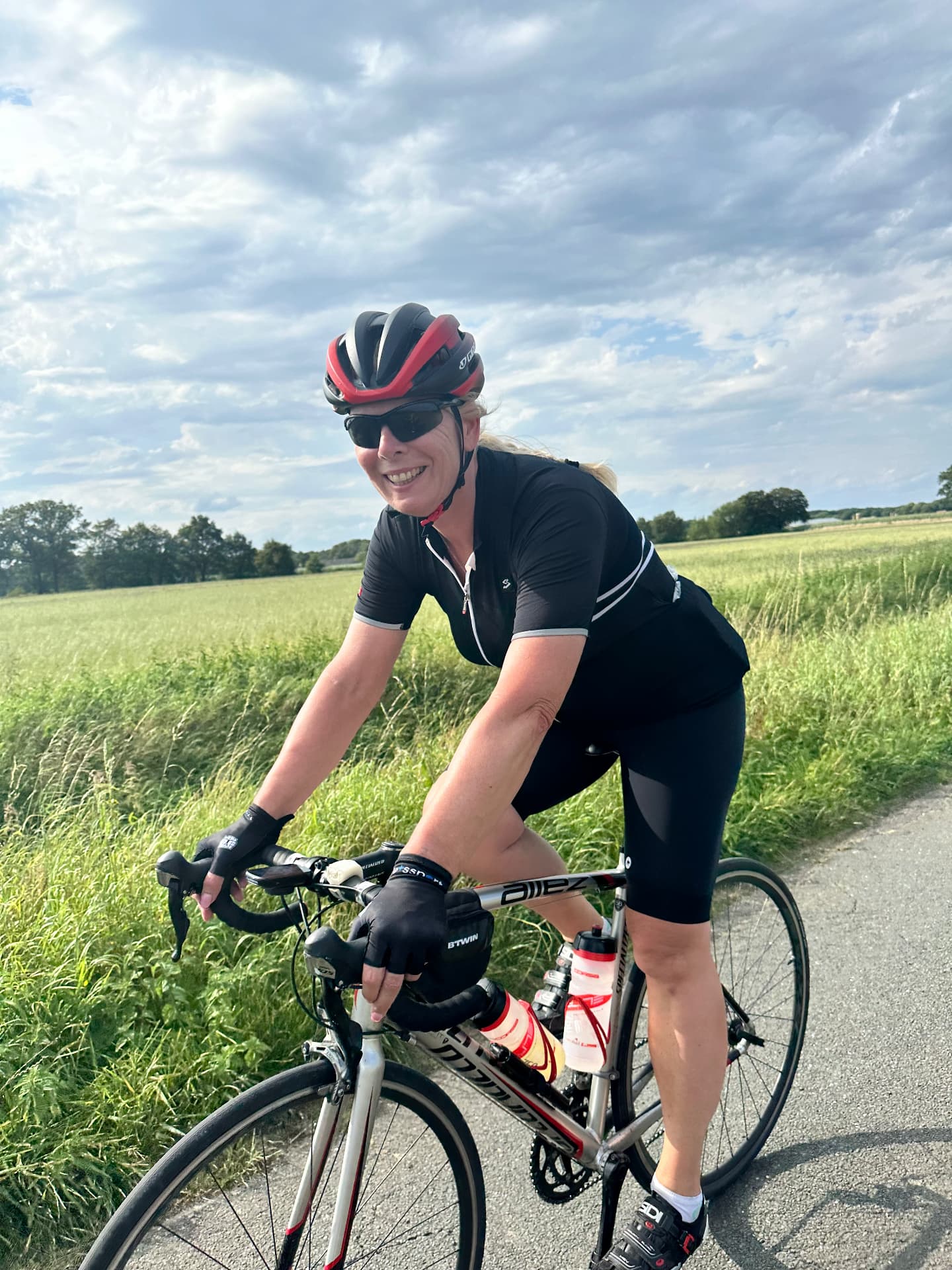 Sfeer van een eerdere Fietsvrouwen-rit: een lachende deelneemster op haar racefiets langs het weiland