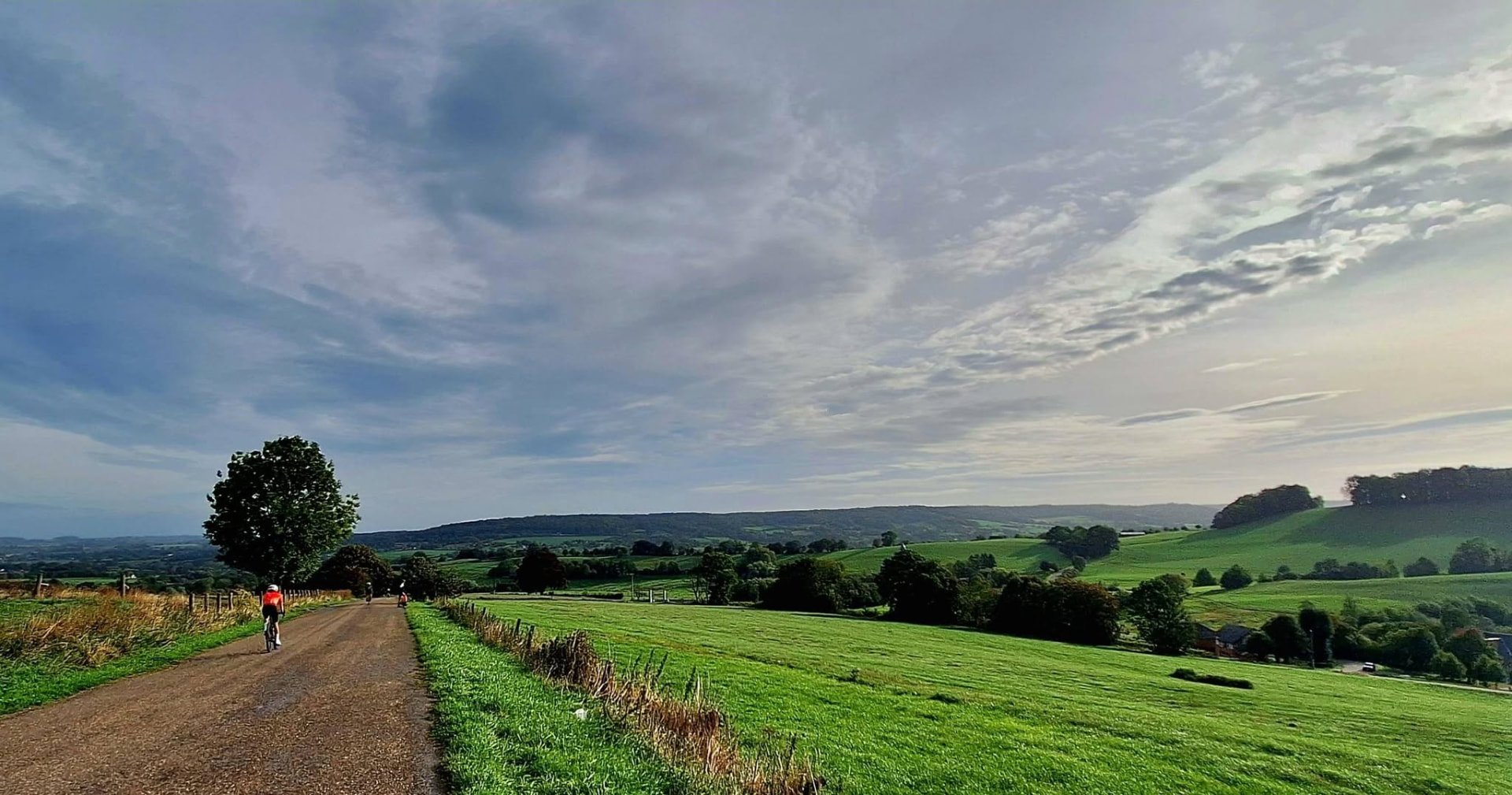 Fietser op een grindpad door het glooiende groene landschap van Zuid-Limburg onder een bewolkte lucht