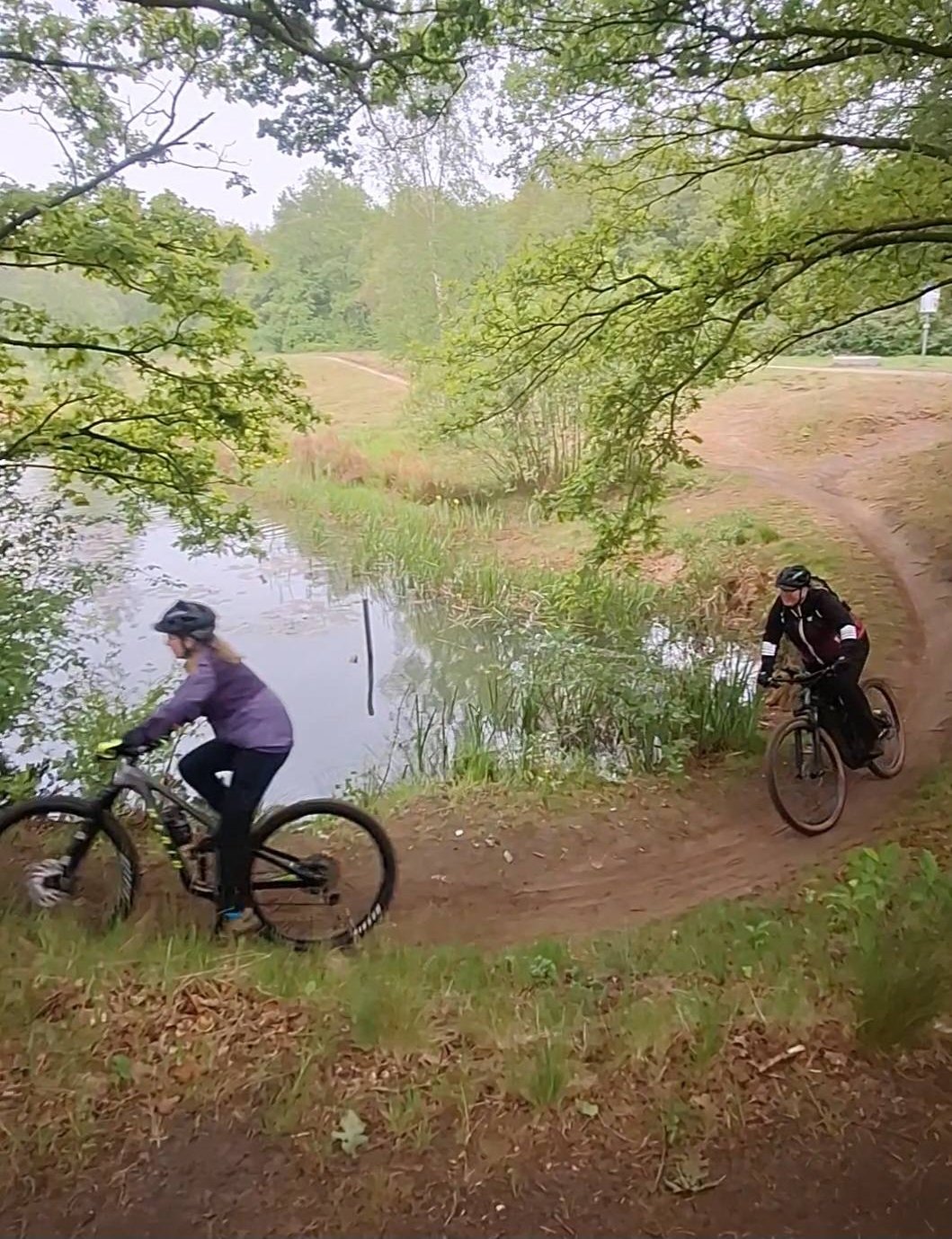 Twee mountainbikesters op een kronkelend pad langs het water bij Assen