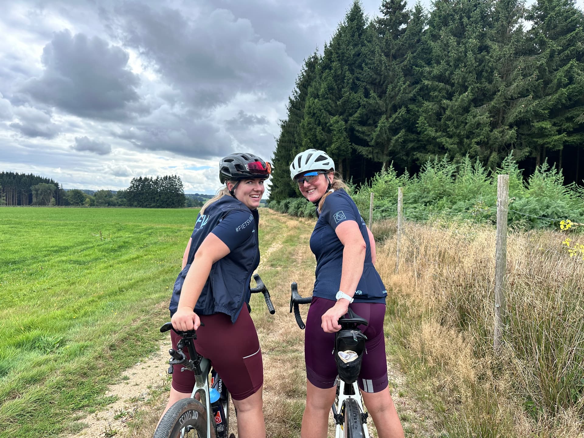 Sfeer van een eerdere Fietsvrouwen-rit in de Ardennen: twee lachende deelneemsters met hun gravelbikes langs een weiland