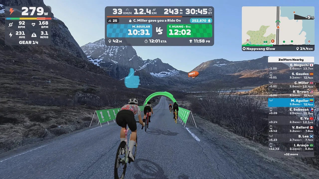 Fietsers in Zwift Video op de route Nappvang Glow op de Lofoten, met besneeuwde bergen en de Zwift-zeppelin