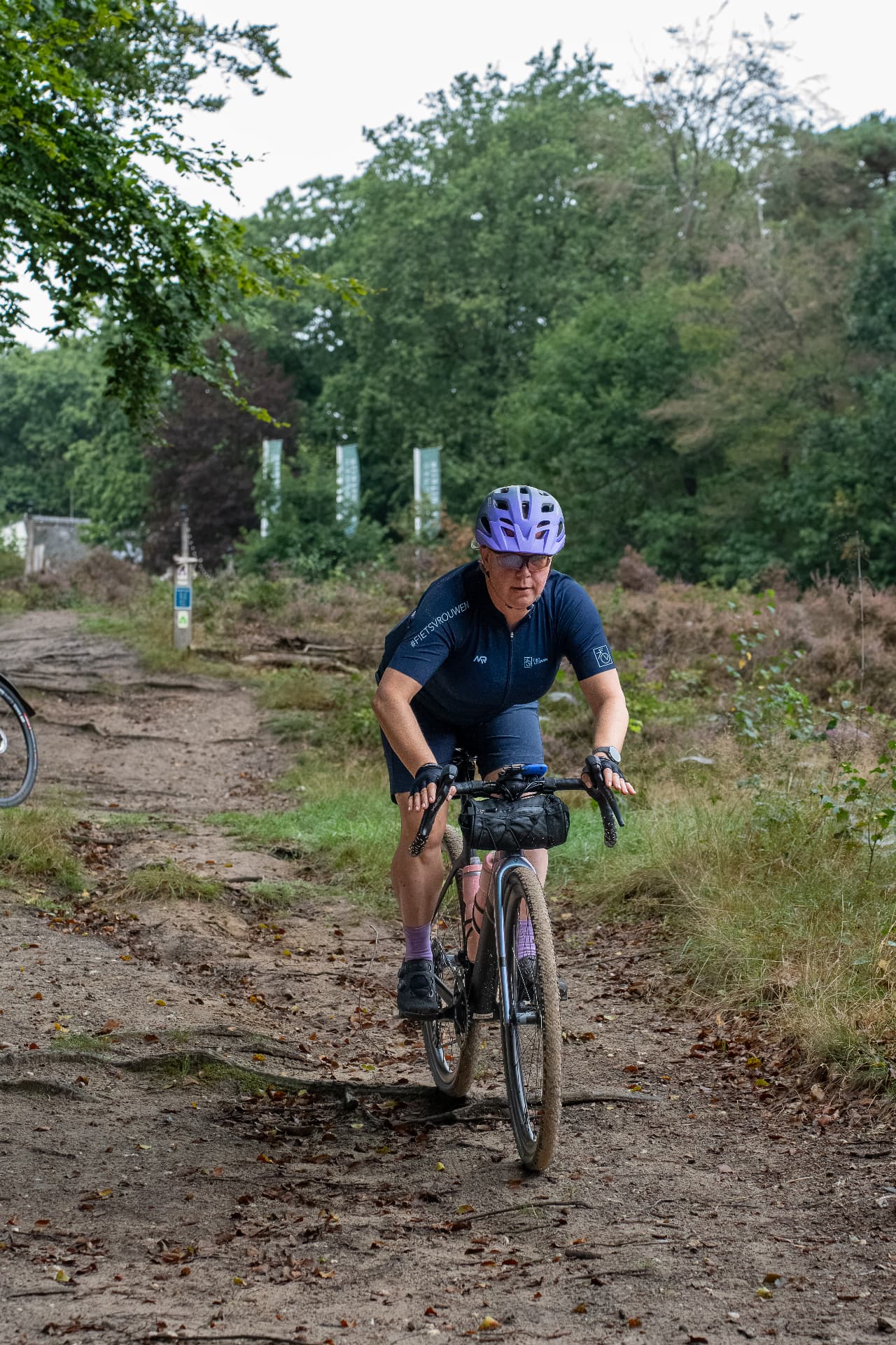 Een lid rijdt alleen met haar fiets over een zandpad door het bos